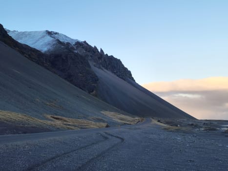 Icelandic rocky landscape on highway, lonely road in nordic wintry weather with empty wilderness. Frozen long road with massive mountain chain and cliffs in iceland, scenic route.