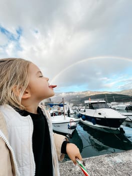 Little girl in profile posing holding a rainbow on her tongue. High quality photo
