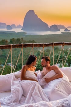 A couple in an outdoor bedroom watching the sunrise over Sametnangshe mountains in Phangnga Bay Thailand