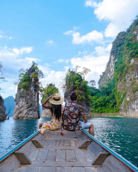 A couple of men and women in front of a longtail boat in Khao Sok National Park Thailand, couple on a boat trip with blue lake and scenic green mountains