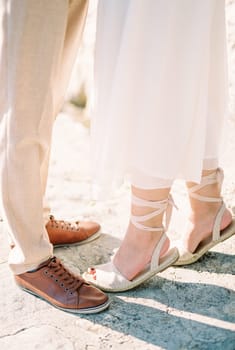 Bride stands on her tiptoes near groom on the road. Cropped. Faceless. High quality photo