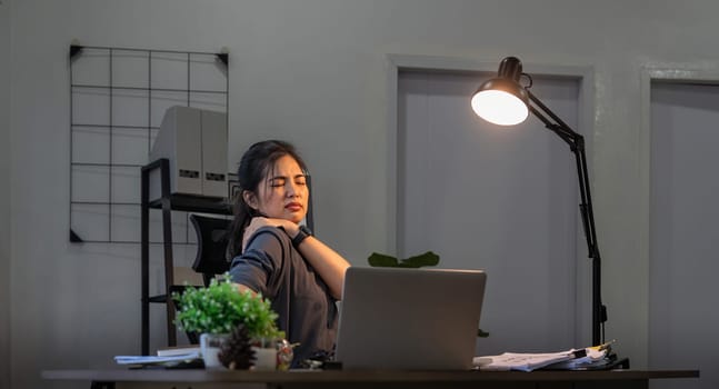 Asian business woman have a neck pain because using the laptop computer and working for a long time at night.