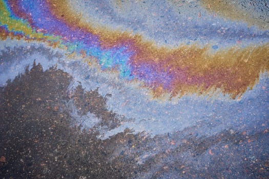 Multi-colored poisonous spots of spilled gasoline on wet pavement during rain. Rain blurred the car oil from a malfunctioning car in a parking lot