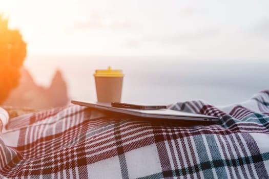 Laptop coffee on blanket with ocean view. Illustrating serene outdoor laptop use. Freelancer enjoying their time outdoors while working or browsing the internet