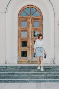 Woman staircase city. A business woman in a white shirt and denim skirt walks down the steps of an ancient building in the city.