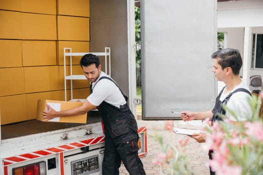 In uniform smiling removal company workers efficiently unload boxes from the truck ensuring a smooth move into a new home. Teamwork and relocation service bring happiness. Moving Day