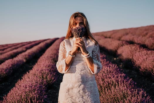 Close up portrait of young beautiful woman in a white dress and a hat is walking in the lavender field and smelling lavender bouquet.