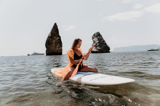 Close up shot of beautiful young caucasian woman with black hair and freckles looking at camera and smiling. Cute woman portrait in a pink bikini posing on a volcanic rock high above the sea