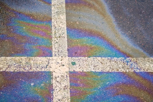 Gasoline spot on wet asphalt. Multi colored oil spill on asphalt road, abstract background, texture.