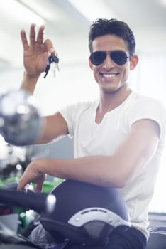 Handsome man, portrait and motorcycle keys with helmet and sunglasses for transportation vehicle in garage. Young male person or biker smile for cool automobile or ownership of mechanical motorbike.