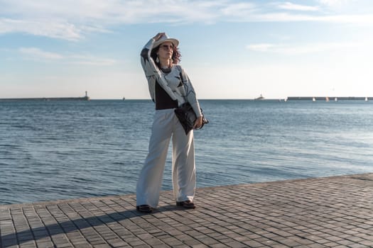 Stylish seashore woman. Fashionable woman in a white hat, white trousers and a light sweater with a black pattern on the background of the sea