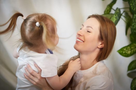 Happy loving family. Mother and daughter child girl playing and hugging in living room with wicker chair