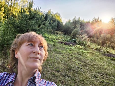 Funny adult girl posing in nature. A middle-aged woman takes a selfie in the landscape. City tourist on vacation on picnic