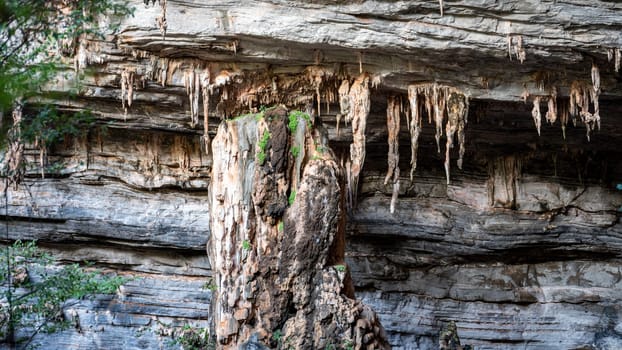 Impressive sight of large stalactites hanging from a cliff outside a natural cave.