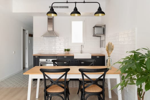 Horizontal shot of black and white kitchen with loft ceiling combined with a dining area overlooking the corridor. Concept of renovation in new building for a young couple.