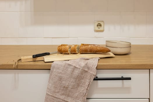 Kitchen tabletop surface with knife and bread on cutting board near bowl. Slicing french bread in kitchen in designated area. Meal preparation