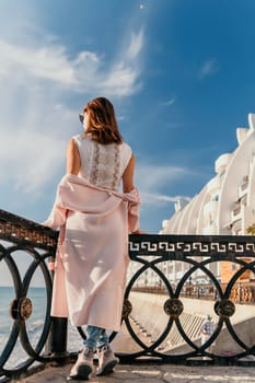 Woman travel sea. Young Happy woman in a long red dress posing on a beach near the sea on background of volcanic rocks, like in Iceland, sharing travel adventure journey