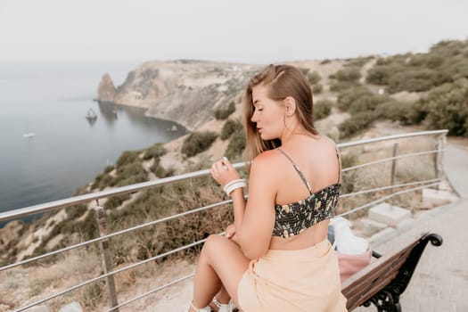 Woman travel sea. Happy tourist taking picture outdoors for memories. Woman traveler looks at the edge of the cliff on the sea bay of mountains, sharing travel adventure journey.