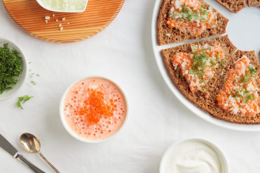 Homemade appetizer with red caviar, sour cream, dill, onion and rye bread on the white table - the traditional finnish recipe for a holiday food, flat lay in minimalistic style, healthy eating concept, horizontal