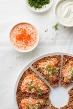 Homemade appetizer with red caviar, sour cream, dill, onion and rye bread on the white table - the traditional finnish recipe for a holiday food, flat lay in minimalistic style, healthy eating concept, vertical