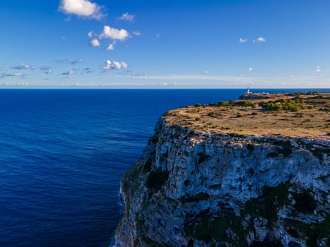 A lighthouse atop a vertical cliff, marking the junction of sea and sky on the horizon.