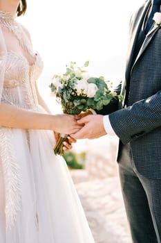 Groom holds the hands of bride with a bouquet of flowers. Cropped. Faceless. High quality photo