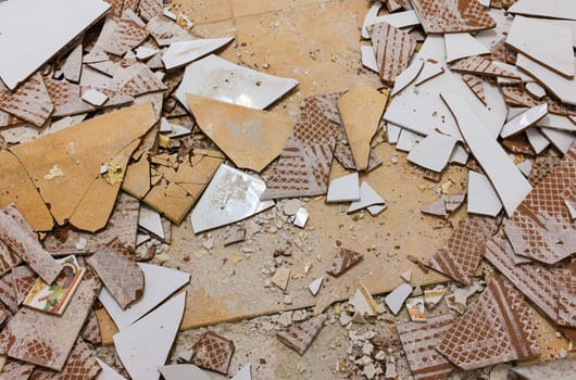 Top view of the floor of a house under demolition with pieces of broken ceramic bricks in shades of white and brown.