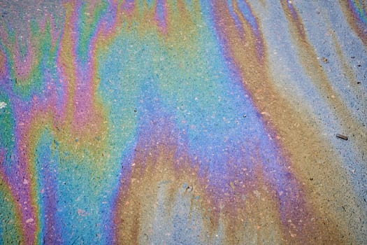 Multi-colored poisonous spots of spilled gasoline on wet pavement during rain. Rain blurred the car oil from a malfunctioning car in a parking lot