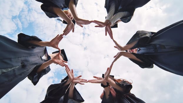 College graduates make a circle of their hands