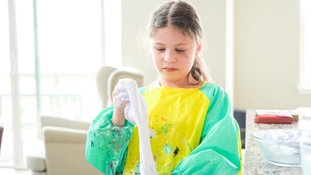 In a modern kitchen, a homeschooled girl is engrossed in creating homemade slime, a fun and educational hands-on project that enhances her creativity and problem-solving skills.