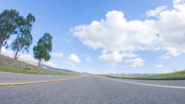 On a clear winter day, a car smoothly travels along Highway 101 near Santa Maria, California, under a brilliant blue sky, surrounded by a blend of greenery and golden hues.