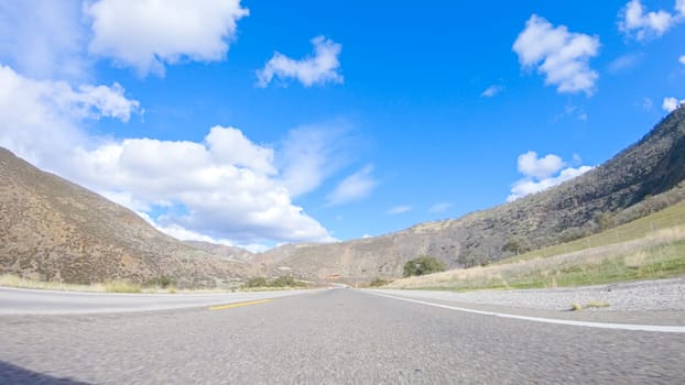 Vehicle is cruising along the Cuyama Highway under the bright sun. The surrounding landscape is illuminated by the radiant sunshine, creating a picturesque and inviting scene as the car travels through this captivating area.