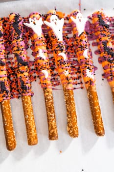 Dipping pretzel rods into melted chocolate to make Halloween chocolate-covered pretzel rods.