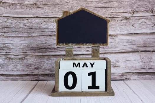 Chalkboard with May 01 calendar date on white cube block on wooden table.