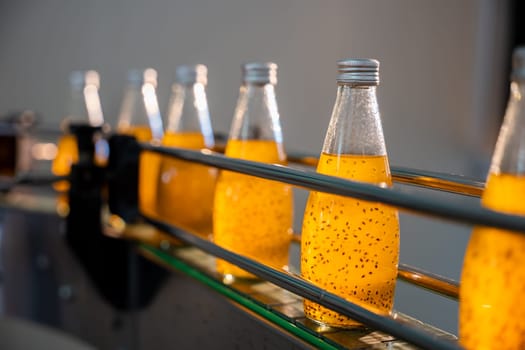 The beverage factory's automated bottling line efficiently fills transparent bottles with organic basil or chia seed drinks blended with pomegranate. Quality production and cleanliness are evident.