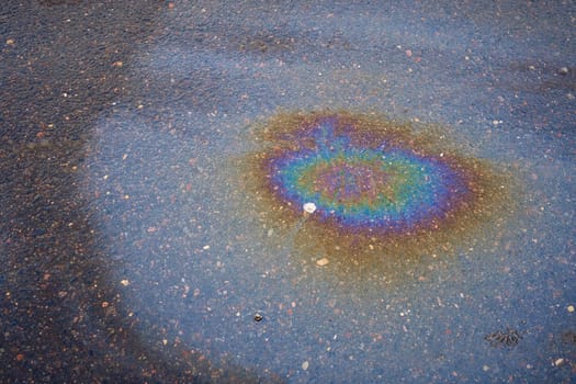 Colorful gas stain on wet asphalt. Oil stain caused by a leak under a car or truck. Environmental pollution concept