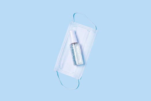 Flat lay with a medical mask placed in the center, a bottle of antiseptic soap or hand sanitizer.