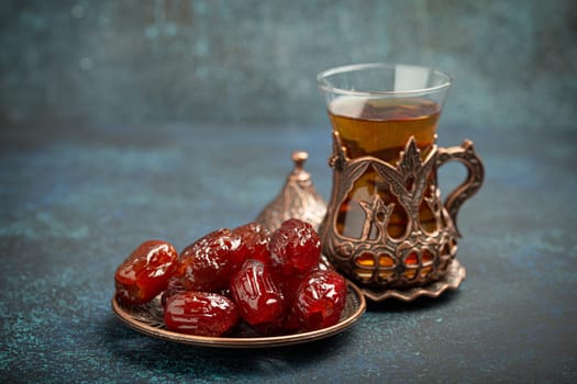 Breaking fasting with dried dates during Ramadan Kareem, Iftar meal with dates and Arab tea in traditional glass, angle view on rustic blue background. Muslim feast.