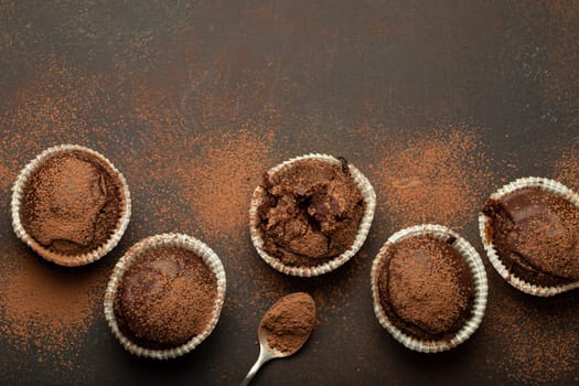 Chocolate browny muffins and cocoa in teaspoon top view on brown rustic stone background, sweet homemade dark chocolate cupcakes.