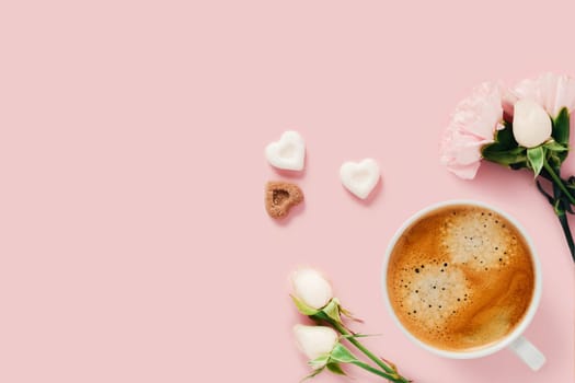 Pink background with a Cup of coffee surrounded by roses and pieces of shugar.