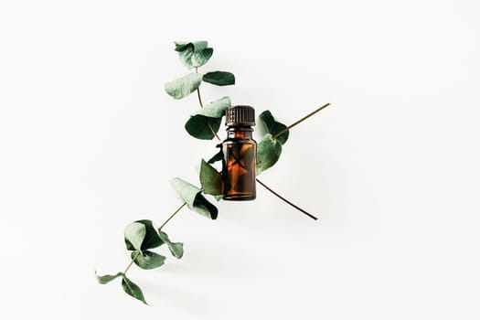 Bottle of fragrant cosmetic or essential oil on a white background surrounded by sprigs of eucalyptus. Stay home and be mentally healthy.