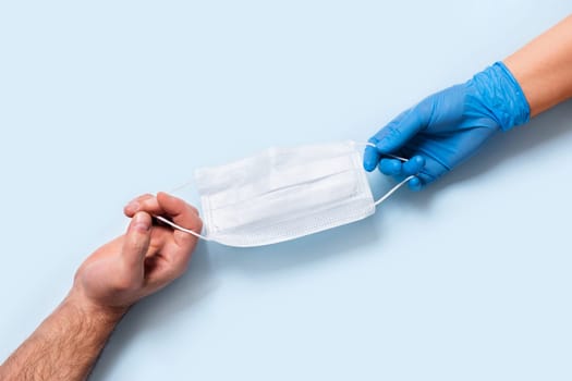 Men's and women's hands in latex gloves holding one medical mask.