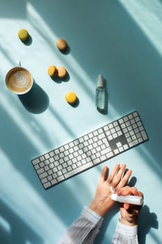 Workplace at home by the window. Flat lat with cup of coffee and macaroons in sunlight and women hands holding a sanitizer.