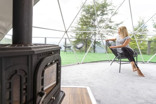 Young woman Rest in the mountains in Glamping. Cozy fireplace in a mountain house.