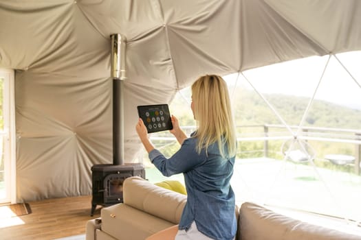 woman holding a tablet with the smart home application in a glamping dome tent domestic.