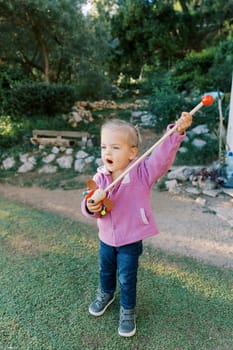 Little girl with a colorful toy on a stick stands on a path in the park. High quality photo