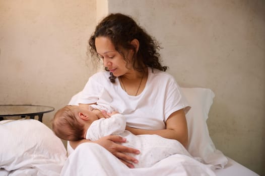 Newborn baby boy sucking milk from mothers breast. Confident portrait of a beautiful woman, young loving mom while breastfeeding baby in cozy home interior. Pregnancy and maternity leave lifestyle