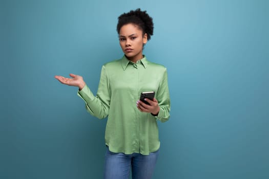 a young brunette hispanic woman with curly hair dressed in a green blouse holds a phone in her hand against the background with copy space. people lifestyle concept.