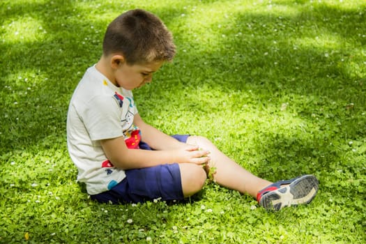 Four year old boy sitting on the grass pensive. Summer day