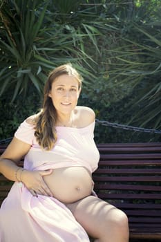 Seven months pregnant woman sitting on a wooden bench. Very happy expression